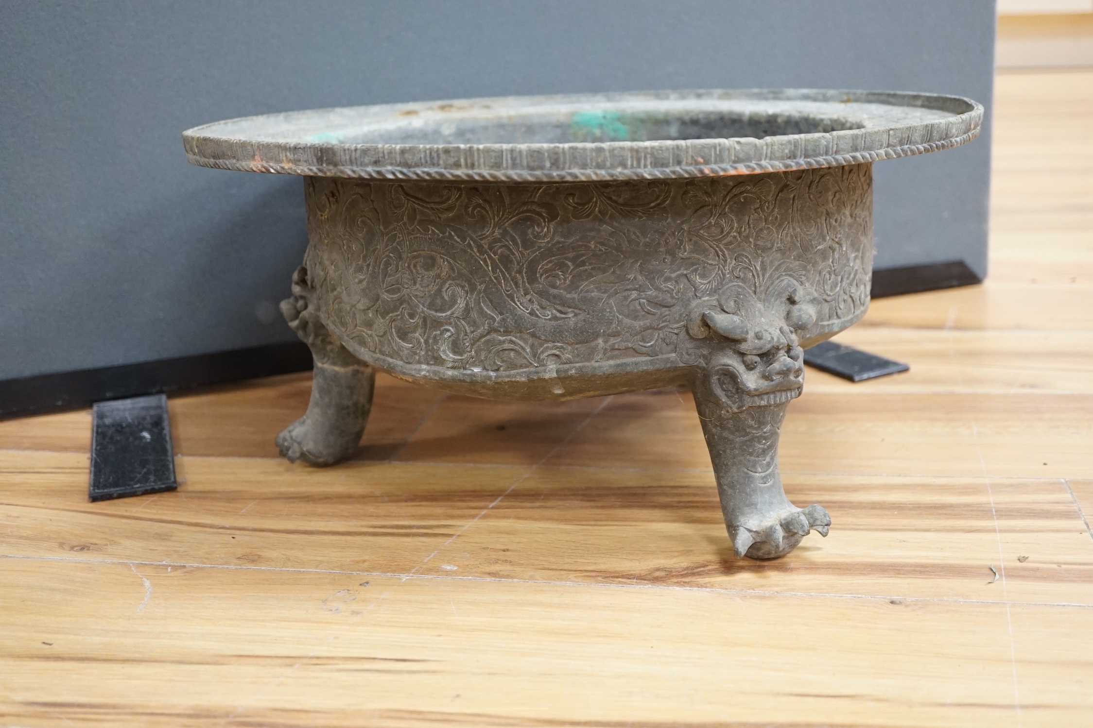 A large and heavy Chinese bronze tripod basin, Xuande mark but 19th century, the broad rim cast in relief with lions, brocaded balls and ribbons, the sides with dragons chasing flaming pearls, on three mythical beast hea
